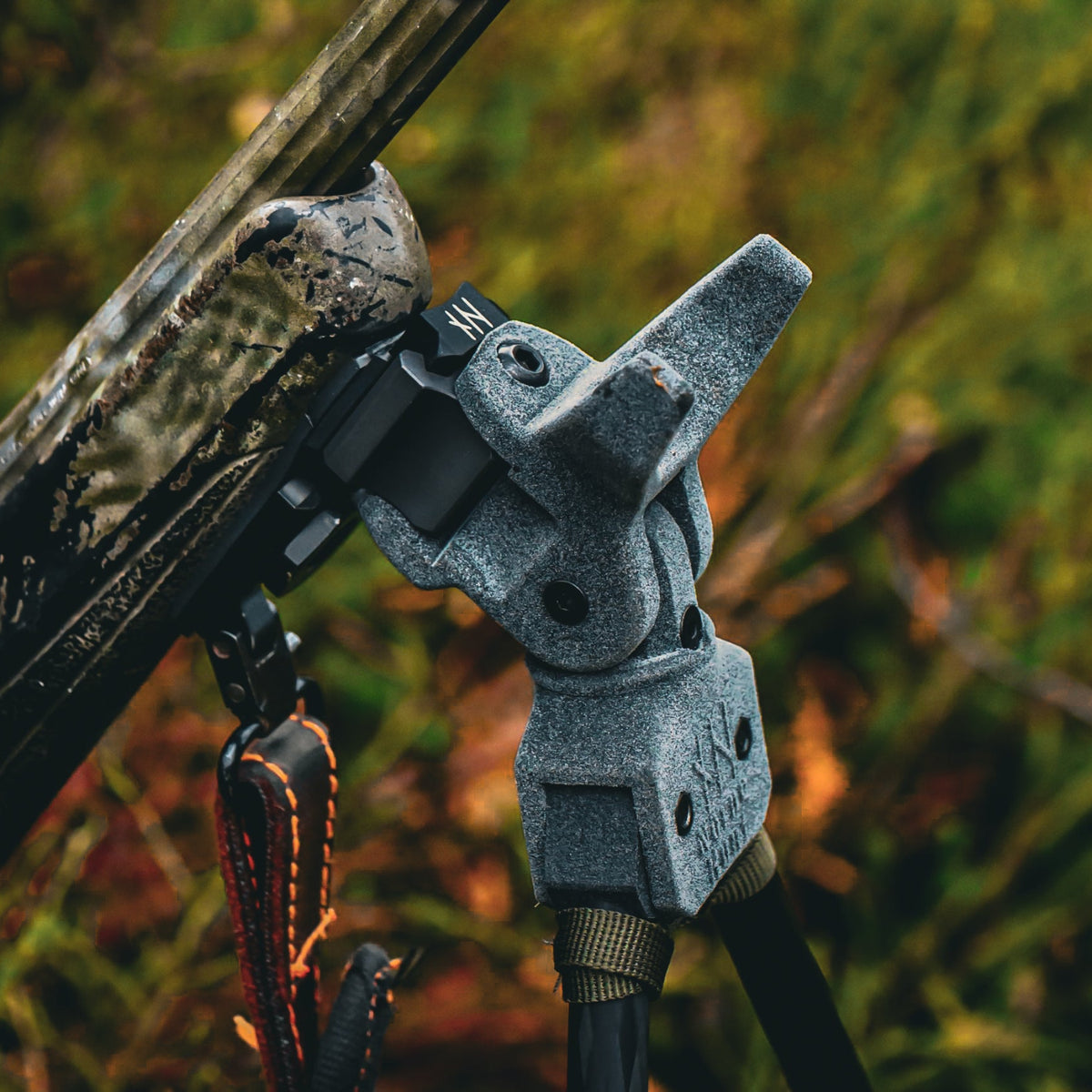 Angled close-up of a NorneHunt shooting stick head connected to a Picatinny rail beneath a camouflage rifle stock.