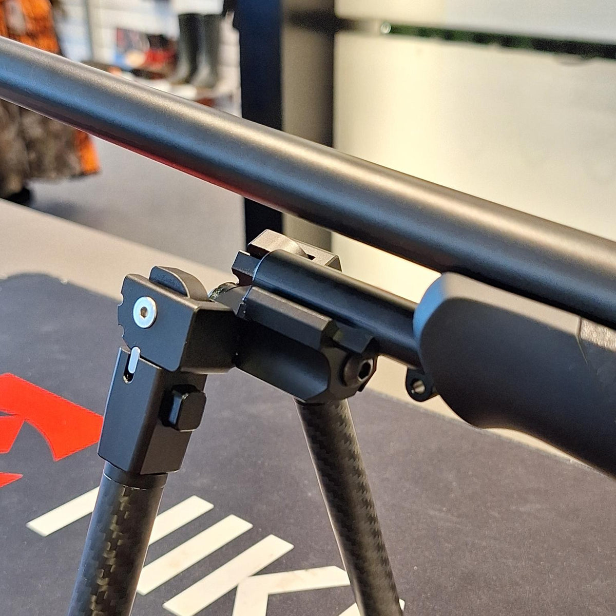 Close-up of a bipod clamp attached to the Sauer 404/505 Picatinny adapter beneath a rifle barrel