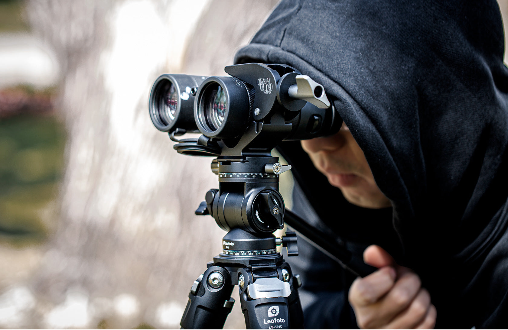 Person using Leofoto BC-02 binocular adapter mounted on a tripod for stable observation in the field.