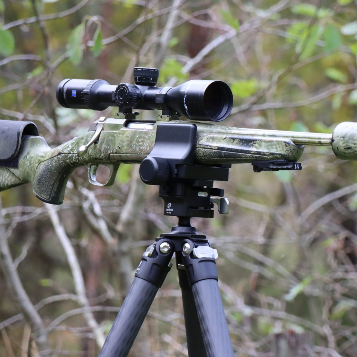 Scoped camouflage rifle held in a Leofoto GS-3 clamp on a carbon fibre tripod in woodland
