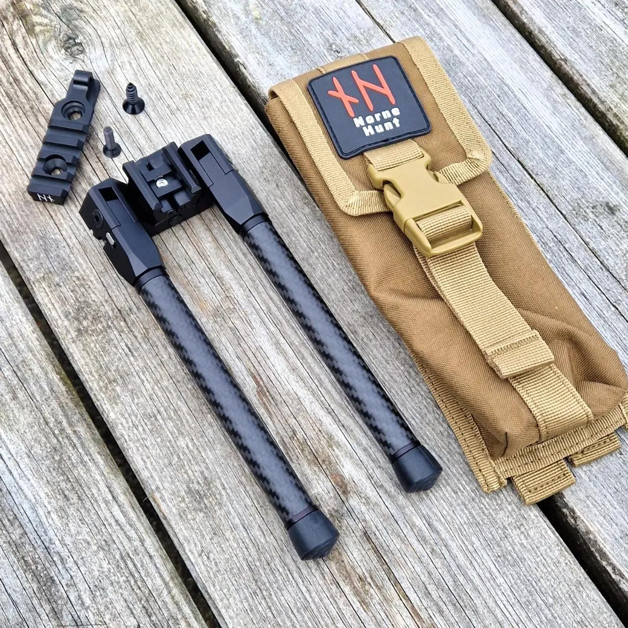 Fmage shows a tactical bipod with carbon fiber legs, a mounting adapter with screws, and a tan carrying pouch featuring a black and red Norne Hunt logo, all arranged on a weathered wooden surface.
